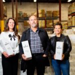 Three Sperri staff stand in a warehouse in front of boxes of their product
